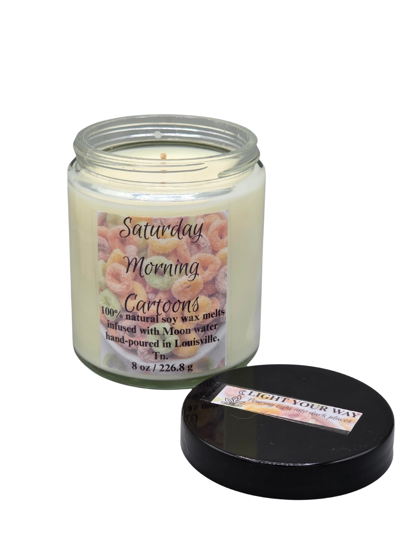 Candle with a label titled 'Saturday Morning Cartoons' and it's black lid off to the side