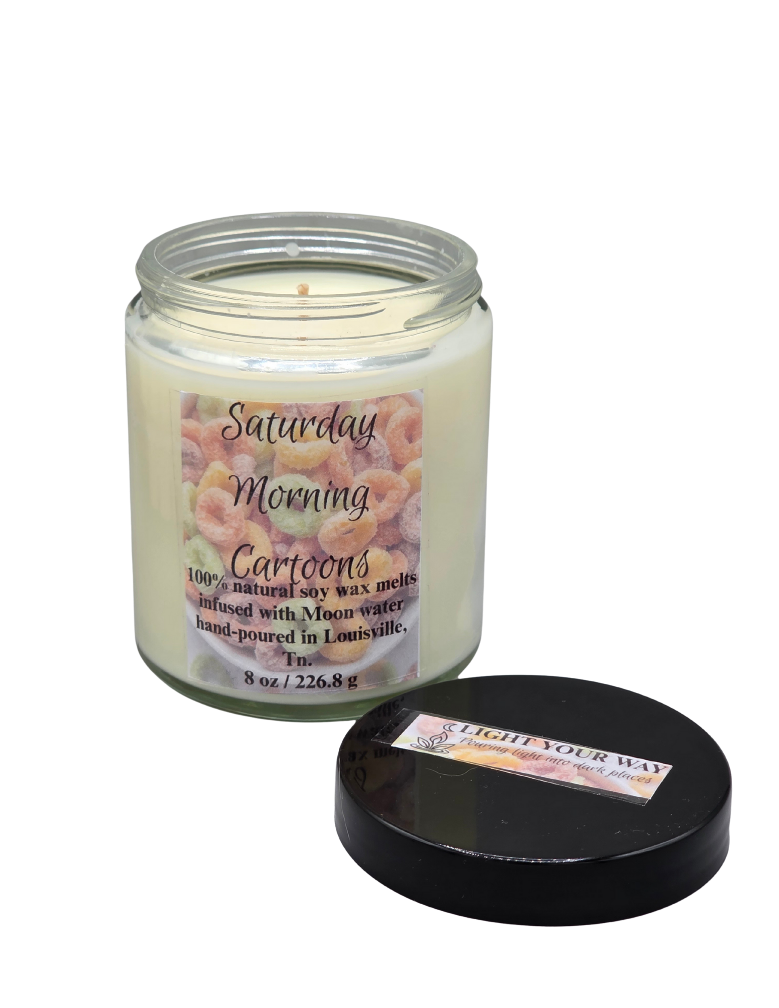 Candle with a label titled 'Saturday Morning Cartoons' and it's black lid off to the side
